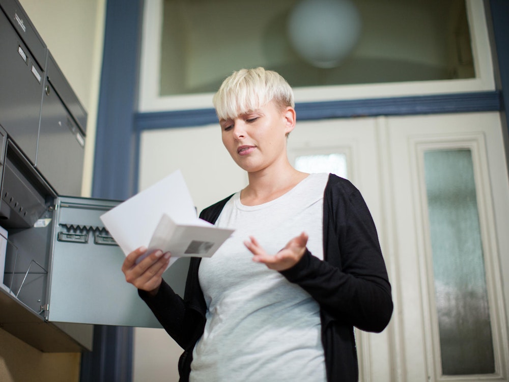 Eine Frau steht mit einem Brief in der Hand vor einem Briefkasten.