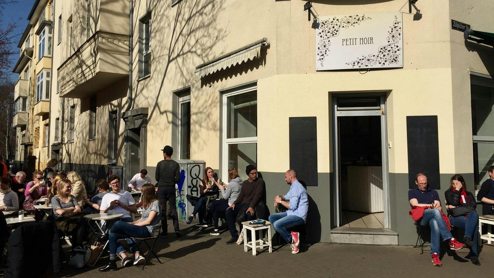 Menschen sitzen auf dem Gehweg vor einem Café