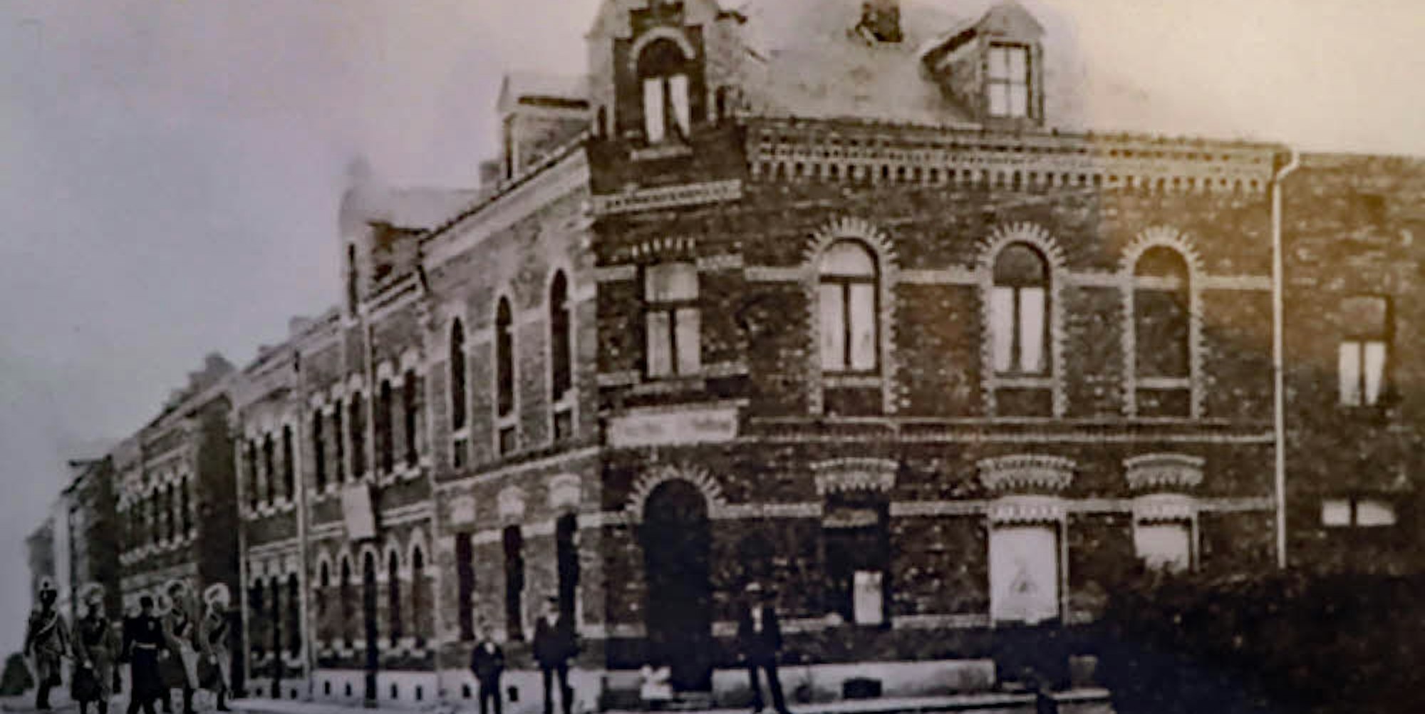 Ein Bild aus dem vergangenen Jahrhundert: Die Hüchelner Straße mit der Gaststätte auf der Ecke. Hinten, neben der Personengruppe, steht das Haus mit der Metzgerei.