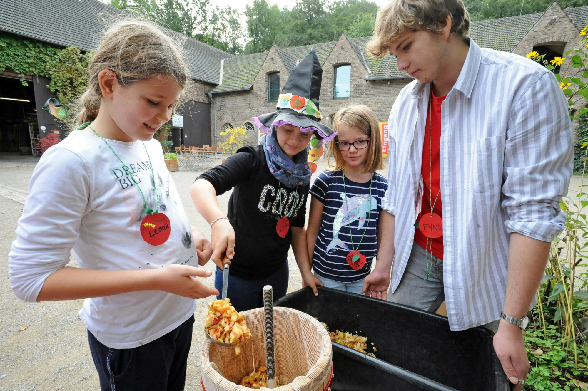 Leonie, Felicitas und Annika geben die geschredderten Äpfel in die Apfelsaftpresse.