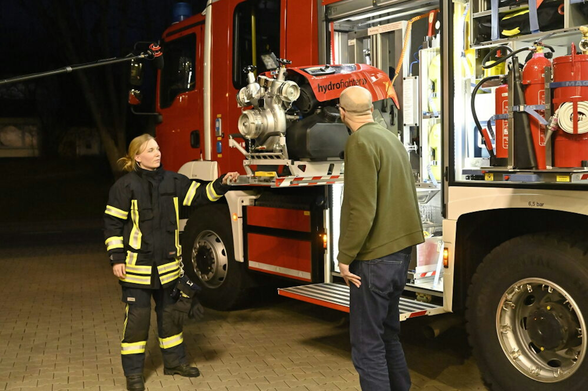 Das Feuerwehrhaus als Studio: Fernsehreporter Matthias Fiedler lässt sich Fahrzeuge und Material der Feuerwehr im und vor dem Feuerwehrhaus in Forsbach erklären, packt selbst mit an und trennt mit der hydraulischen Schere eine Metallstange durch (o.l.).
