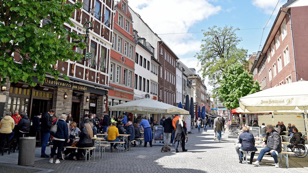 Gäste sitzen draußen an Bierbänken vor der Brauerei "Zum Schlüssel" (l) in der Düsseldorfer Altstadt.