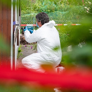 Ein Beamter der Spurensicherung öffnet in Münster in einer Kleingartenkolonie die Tür zur Laube des vermutlichen Haupttäters.