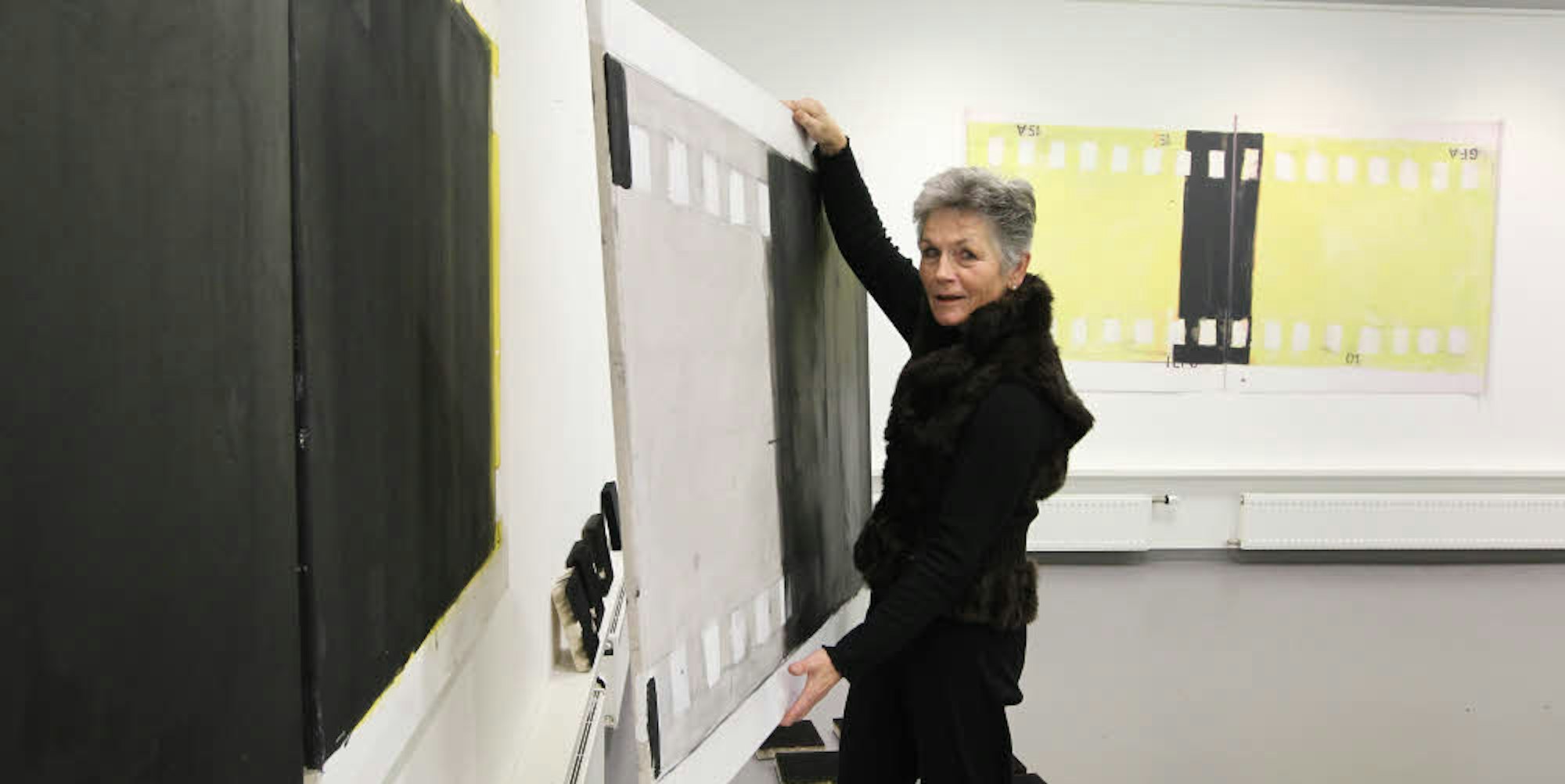 Ilse Wegmann beim Hängen ihrer Arbeiten im Troisdorfer Kunsthaus. Rechts ein Objekt mit Schattenwurf: überdimensionale Filmstreifen aus Pappe