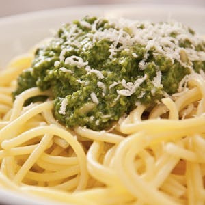 Ein Teller mit Spaghetti und grünem Pesto, darauf Parmesankäse