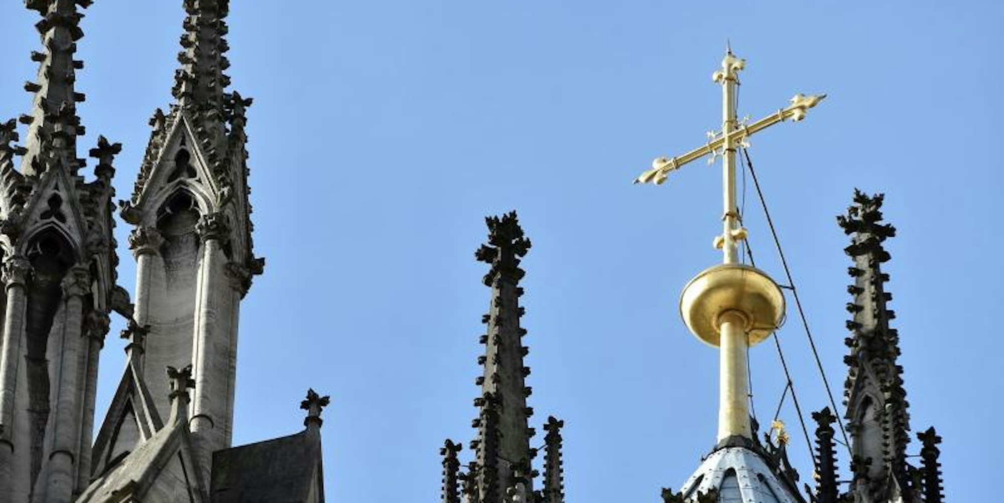 Ein goldenes Kreuz auf dem Kölner Dom leuchtet in der Sonne. 