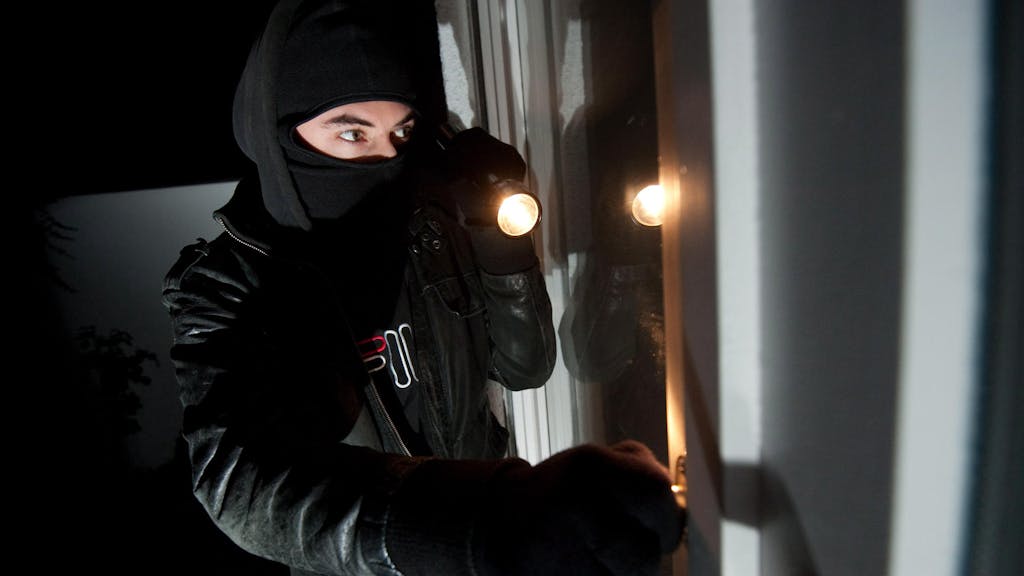 Ein vermummter Einbrecher leuchtet mit einer Taschenlampe in eine Wohnung.&nbsp;