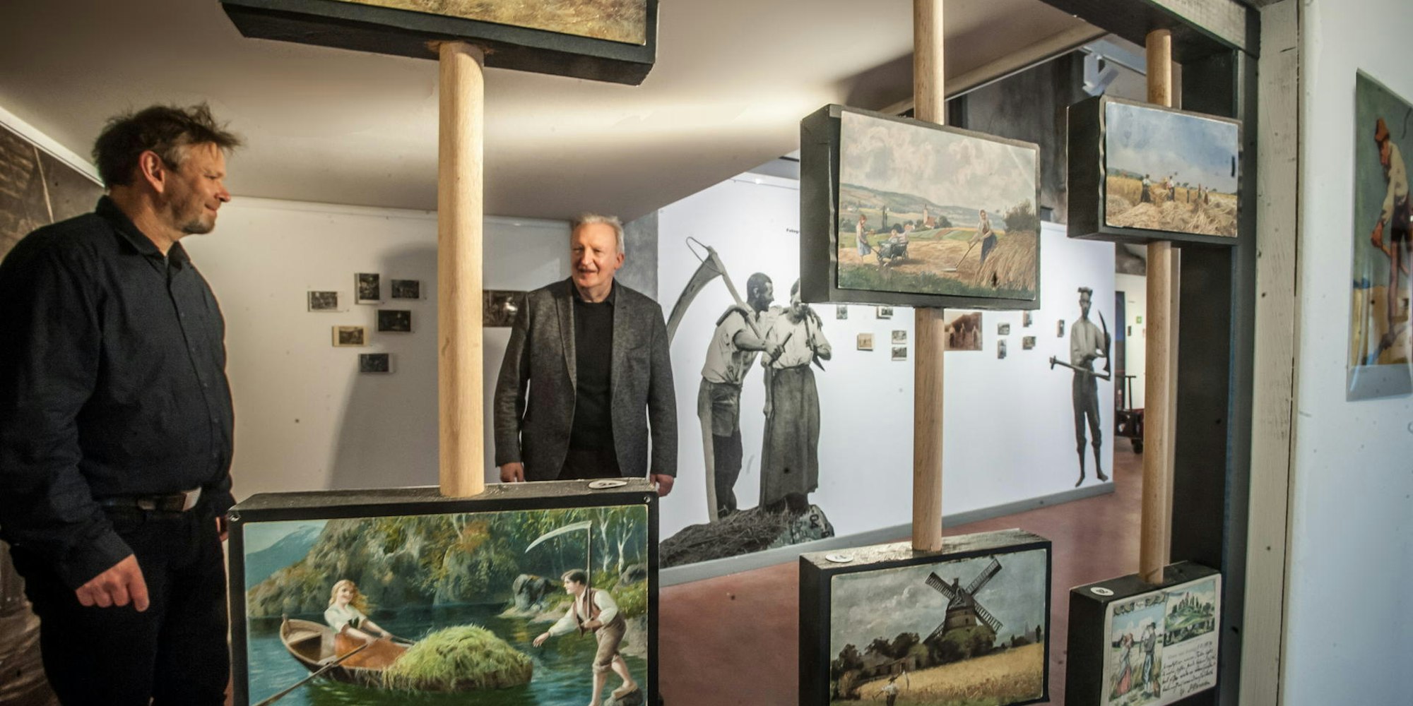 Sensen in allen erdenklichen Variationen auf Postkarten: Jürgen Bandsom (l.), Leiter des Sensenhammers, und Hans Schmitz vom Literaturbüro Leverkusen begutachten die Ausstellung.