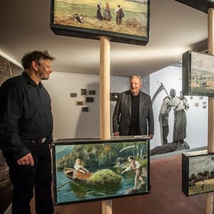 Sensen in allen erdenklichen Variationen auf Postkarten: Jürgen Bandsom (l.), Leiter des Sensenhammers, und Hans Schmitz vom Literaturbüro Leverkusen begutachten die Ausstellung.