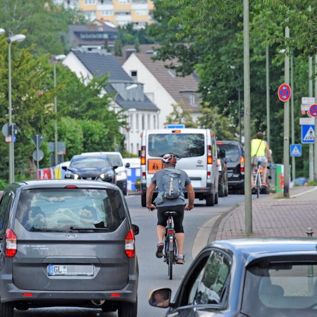Autos, Kleinbus und Radfahrer auf einer Straße.