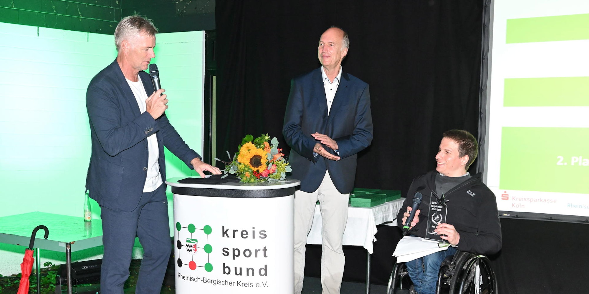 Dr. Marc Schuh mit Hans-Jörg Schneider von der LG Wipperfürth (Mitte) und Moderator Tom Bartels von der ARD auf der Bühne 2021 beim Festakt, bei früheren Ehrungen auf der Bühne im Löwen und beim Training im Stadion in Gladbach.
