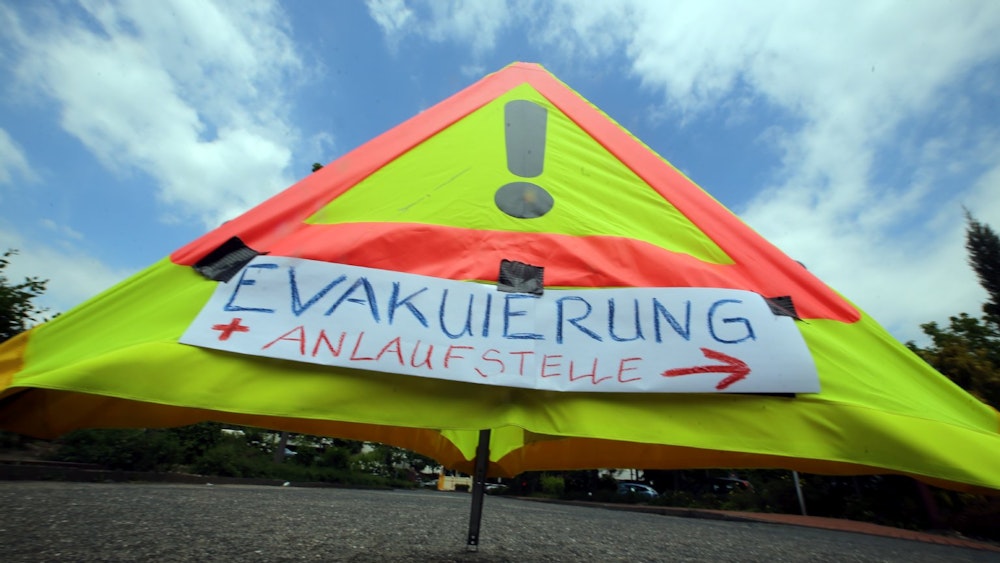 Ein Warnschild mit der Aufschrift „Evakuierung und Anlaufstelle“ steht auf dem Asphalt.