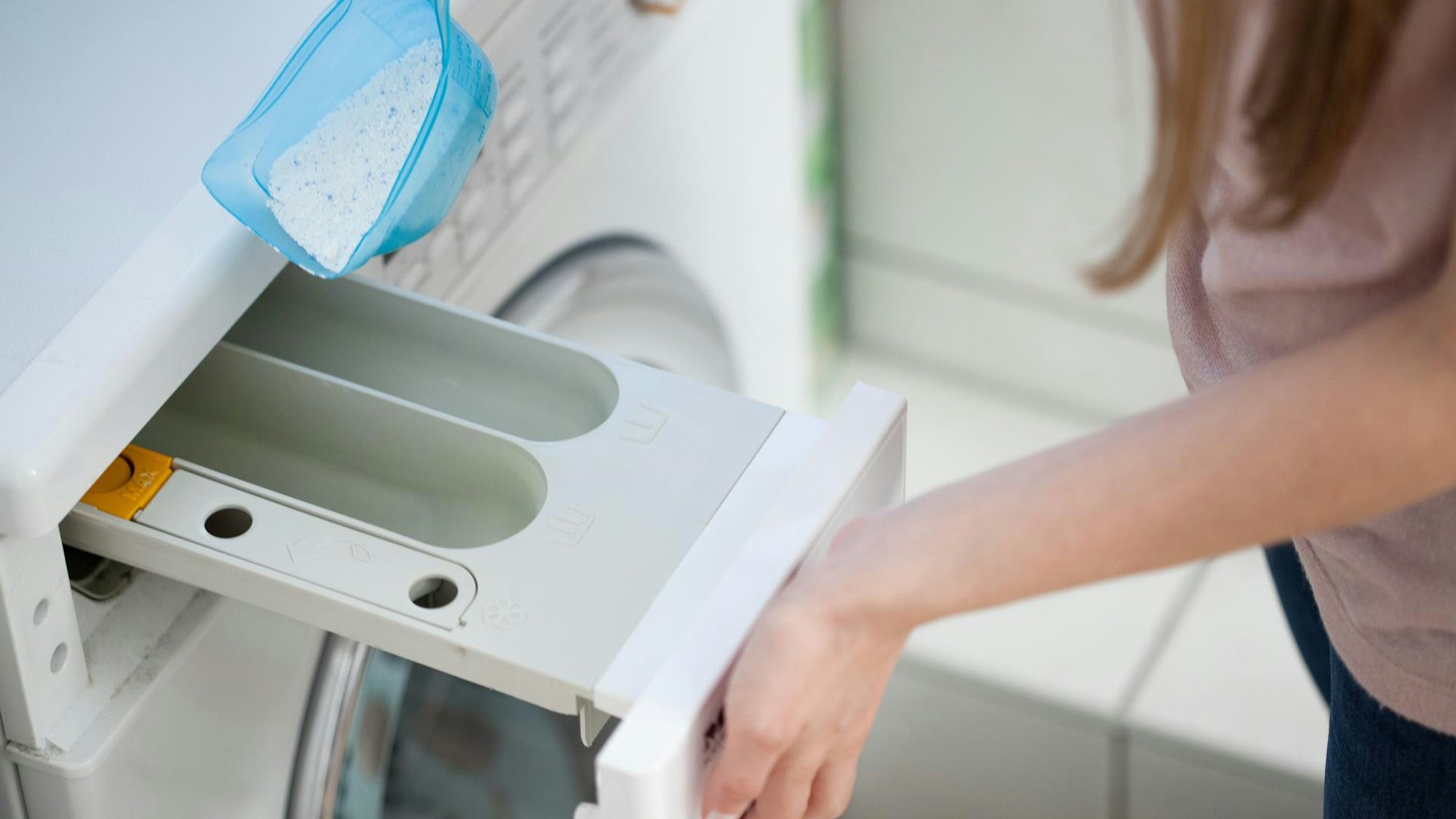 Eine Frau füllt Waschmittel in eine Waschmaschine