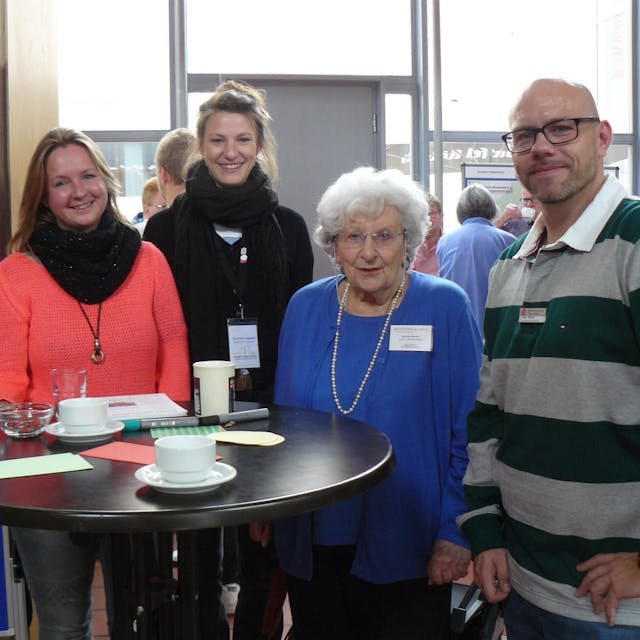 Teilnehmer der Zukunftskonferenz gruppierten sich um die Tische, darunter: Die Blumenbergerin Sarah Simon (v.l.), Corinna Joppien (Quartiersmanagerin in Chorweiler-Mitte), Vera van Beveren (IG Blumenberg) und Sozialraumkoordinator Benjamin Stieb.