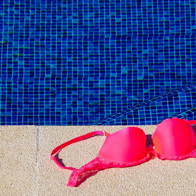 Ein Bikinioberteil liegt am Rand von einem Schwimmbecken.