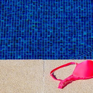 Ein Bikinioberteil liegt am Rand von einem Schwimmbecken.