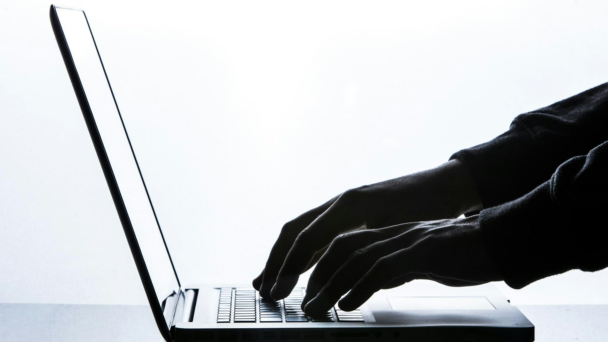 Hände in Handschuhen tippen auf der Tastatur eines Laptops.