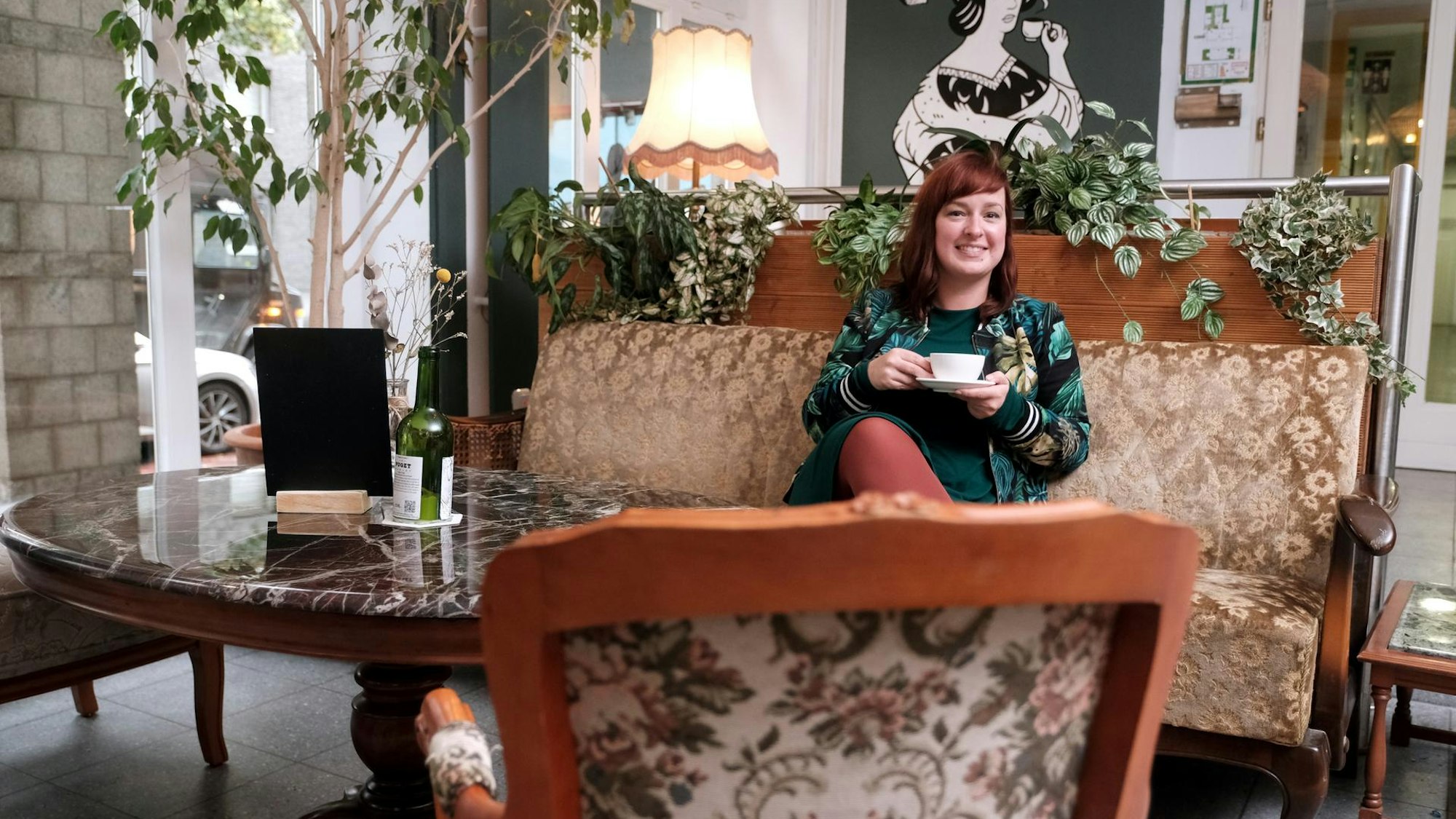 In der Villa Kalka: Julia Floß trinkt Kaffee auf einem Sofa mit Holzrahmen und Samtbezügen.