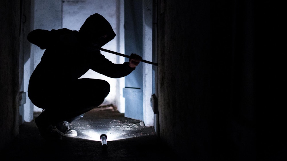 Das Symbolfoto zeigt einen Einbrecher mit Brechstange und Taschenlampe.