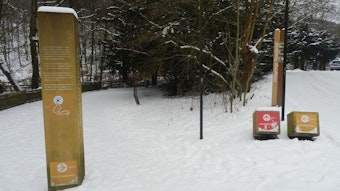 große gelbe Säule mit Texte links, rechts ein roter und ein gelber Würfel mit Pfeilen, auf dem Boden liegt Schnee