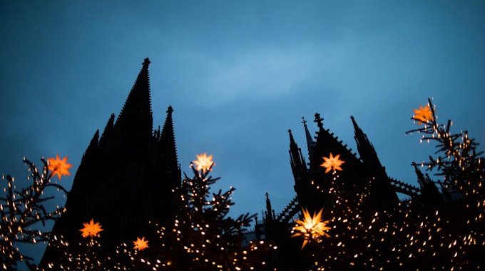 Der Kölner Dom in der Dämmerung, halb verborgen hinter Lichterketten und Weihnachtsbäumen.