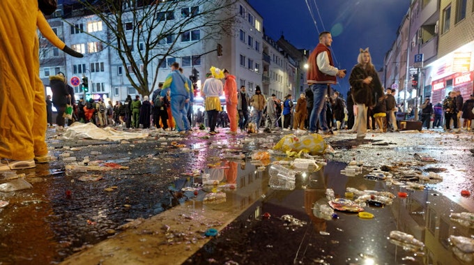 Müll liegt am späten Abend auf der Zülpicher Straße, im Hintergrund stehen kostümierte Menschen in kleinen Gruppen zusammen.