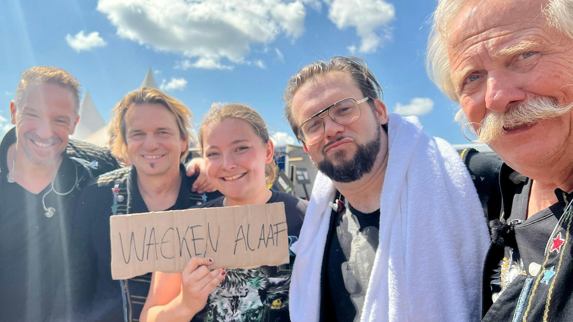 Fans halten ein Schild hoch mit „Wacken Alaaf“: Kölsche Musik trifft Heavy Metal. Rechts im Bild ist Henning Krautmacher zu sehen.