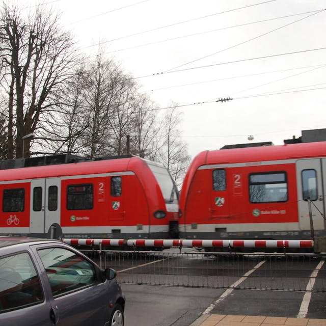 Bahnübergang Brückenstraße in Eitorf, ein Regionalzug fährt durch, während ein Auto vor der Schranke steht.&nbsp;