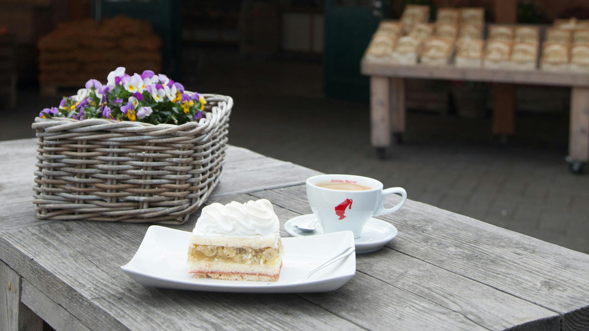 ein Stück Kuchen und eine Tasse Kaffee stehen neben einer Blume auf einem Holztisch
