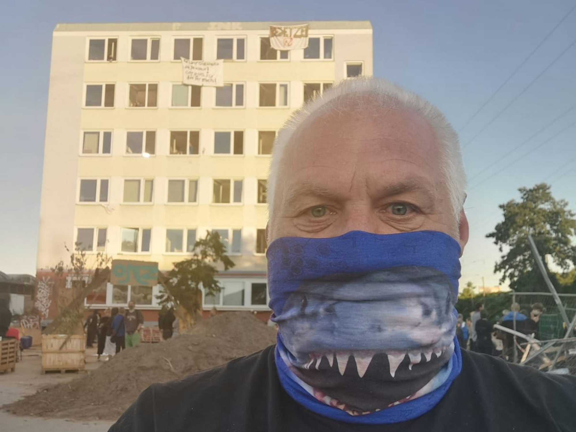 Ein Mann steht mit einem Tuch vor dem Mund vor einem Gebäude.