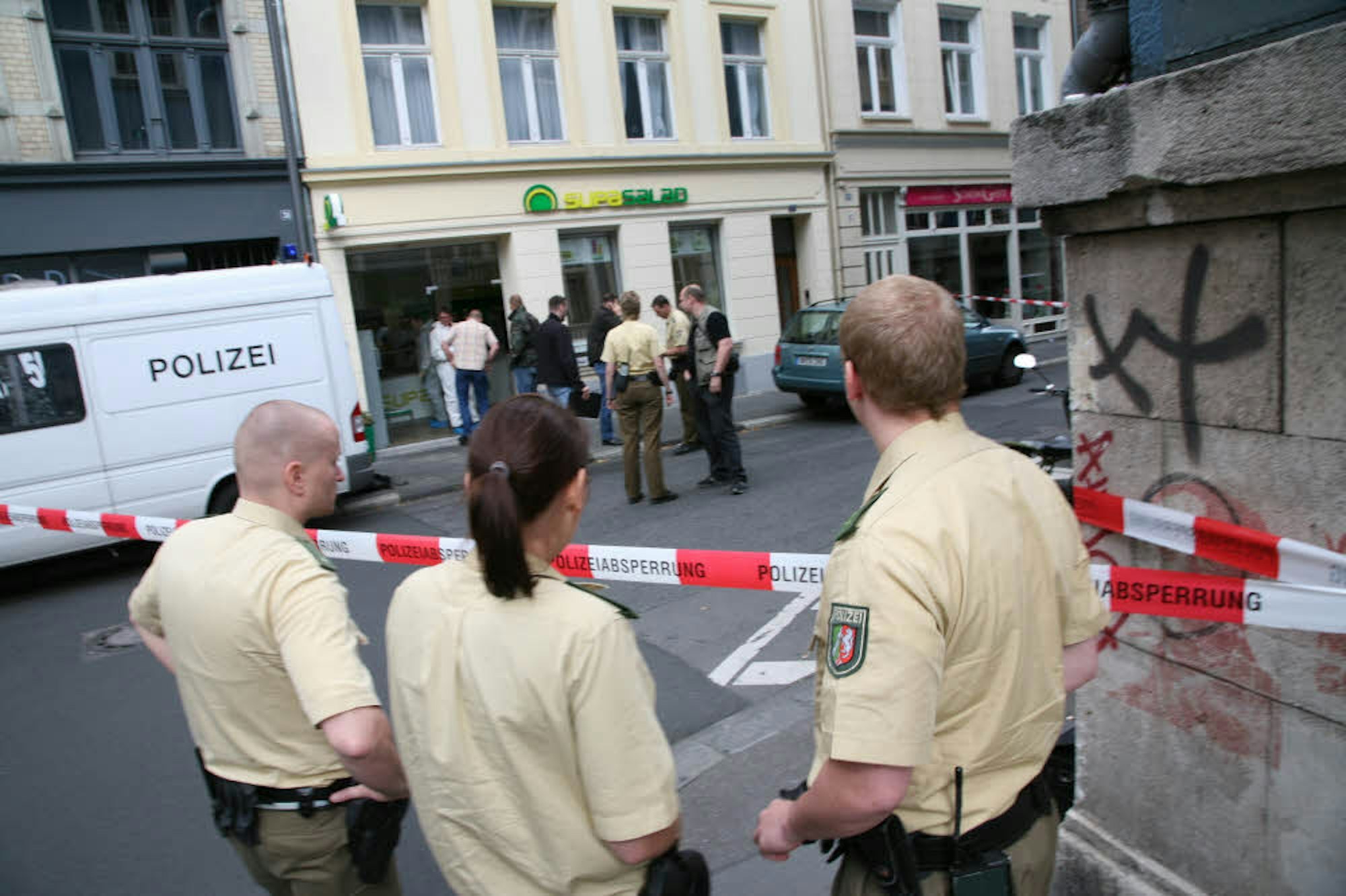Juli 2007, Gertrudenstraße in Köln: Nach einem Leichenfund in der Salatbar „Supasalad“ hat die Polizei den Tatort abgesperrt, um ungestört arbeiten zu können. Anwohner, Passanten oder Journalisten haben keinen Zugang.