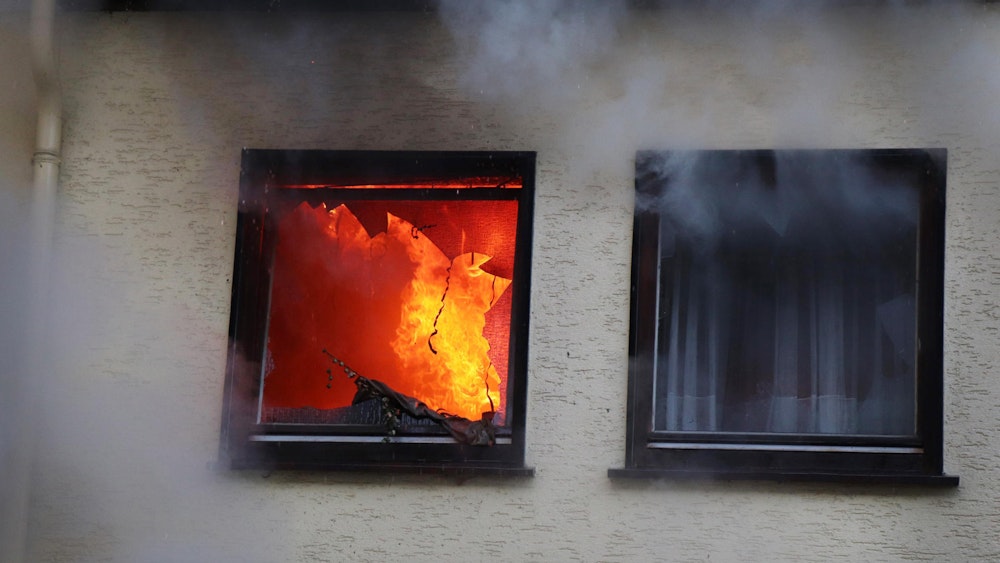 Durch ein Fenster einer Wohnung dringt Rauch, im Innern schlagen Flammen.