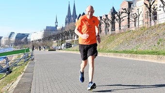 Mann joggt am Rheinufer, Kölner Dom im Hintergrund