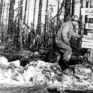 Ein amerikanischer Soldat an einem Wegweiser voller Schilder: Hier verlief 1944 die Frontlinie zwischen deutschen und alliierten Truppen.