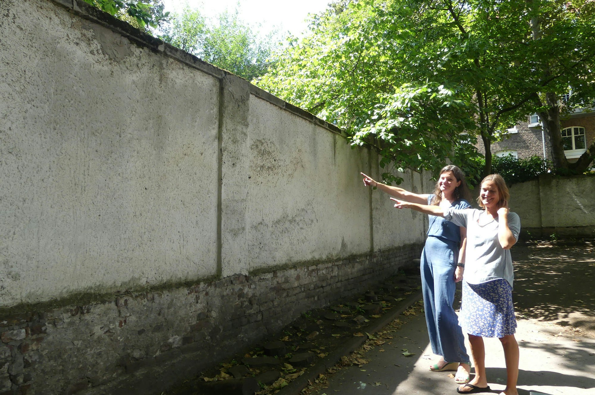 Die Schülermütter Marion Linz (l.) und Anne Rummer zeigen auf die Mauer, hinter der Platz für eine Schulerweiterung wäre.