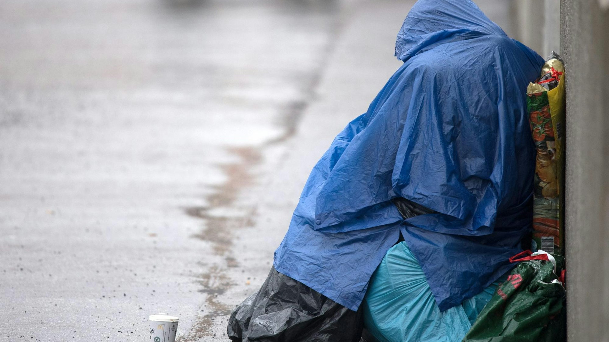 Ein obdachloser Mensch sitzt im Regen am Straßenrand.