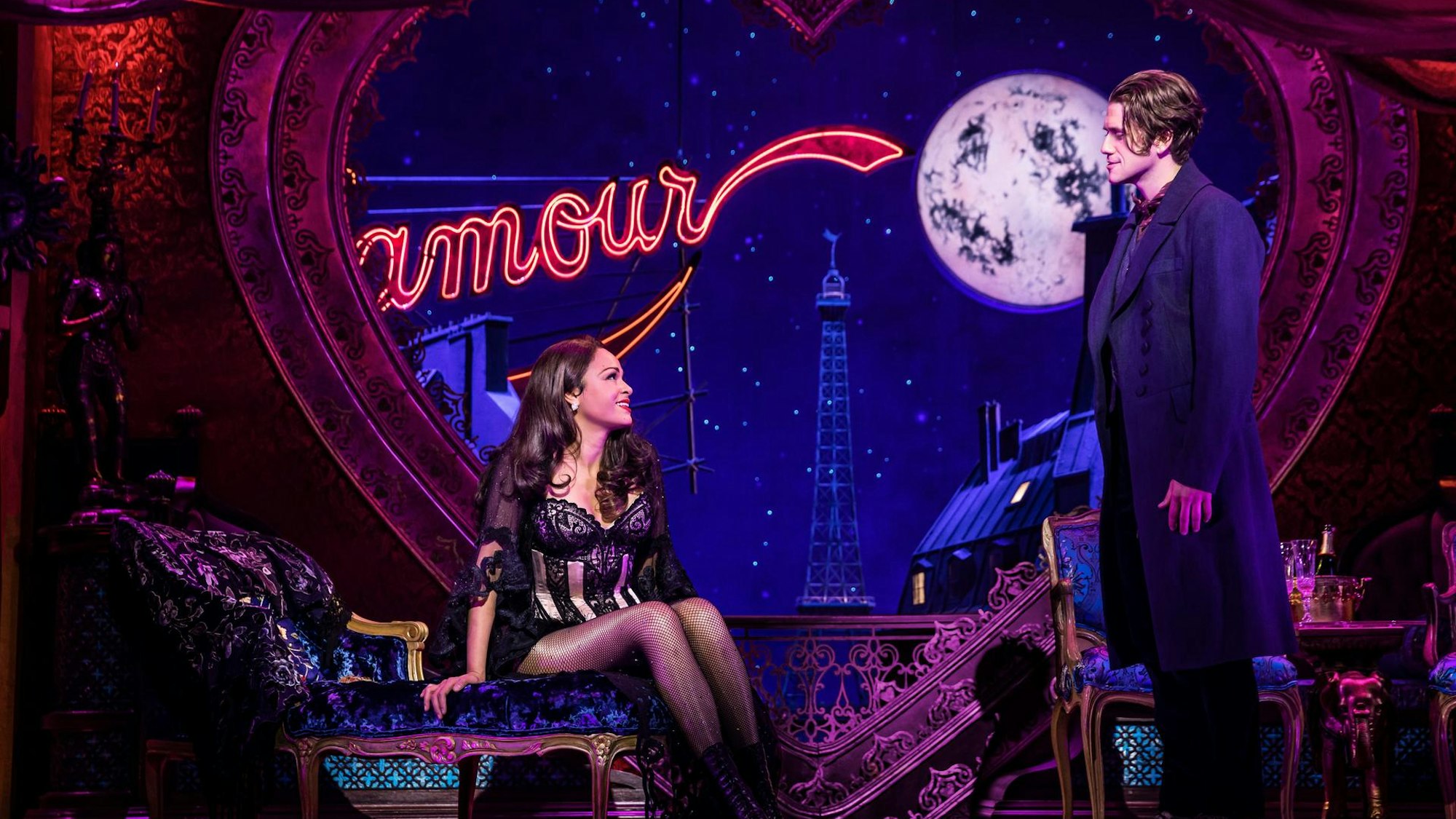 Die beiden Hauptdarsteller von Moulin Rouge in der Kulisse. Sie tragen Kostüme und lachen sich verliebt an.