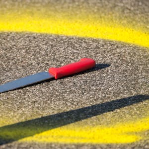 Ein Kreis aus gelber Farbe ist um ein Messer, das auf einer Straße liegt, gemalt.