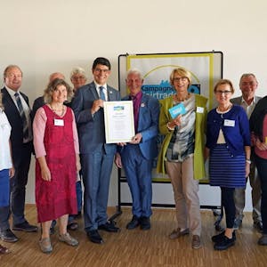 Bürgermeister Klaus Schumacher nimmt zusammen mit der Aktionsgruppe die Auszeichnung vom Fairtrade-Ehrenbotschafter Dr. Manfred Holz entgegen.