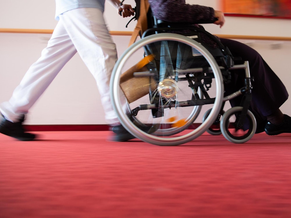 Ein Pfleger schiebt einen Rollstuhl