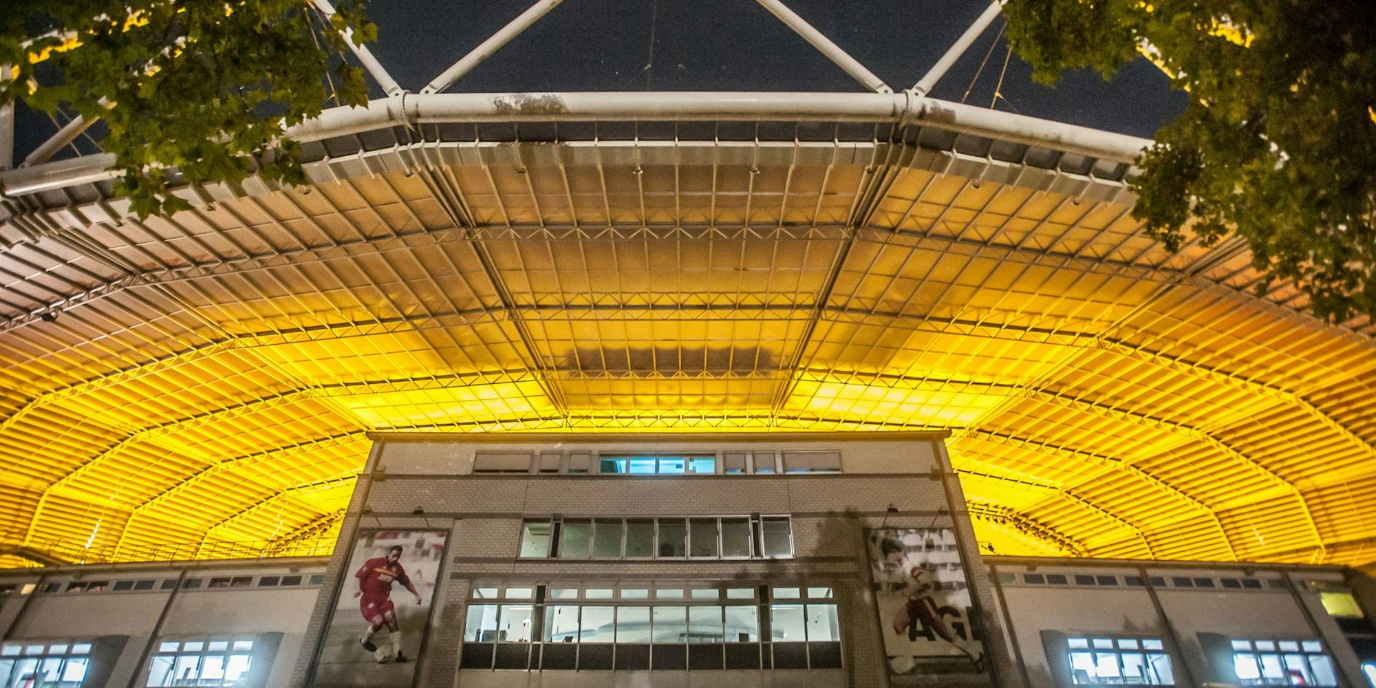 Blick von außerhalb des Stadion: Nachts reflektiert das Kunststoffdach das goldene Streulicht der Wachstumslampen auf dem Spielfeld.