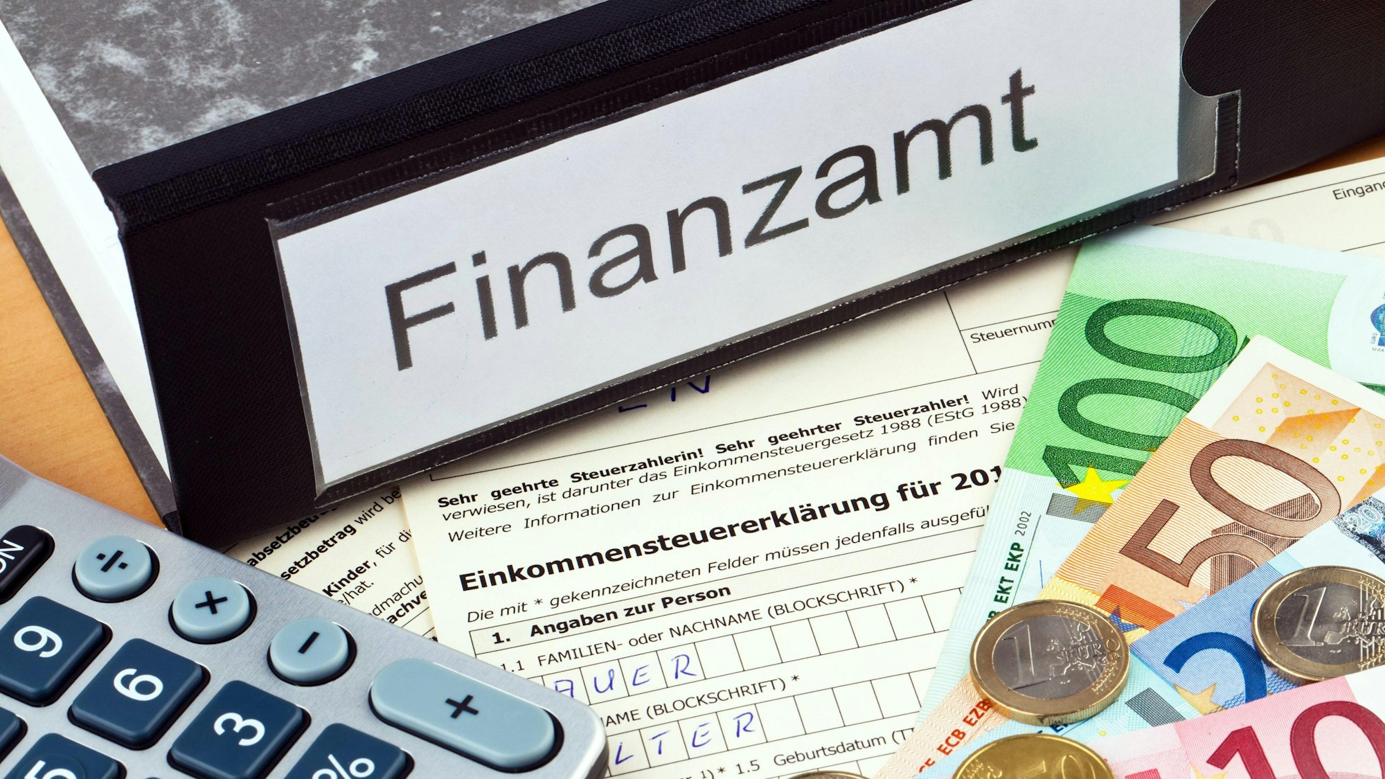 Steuerunterlagen des Finanzamts sind auf einem Symbolbild zu sehen sowie Bargeldscheine und ein Taschenrechner.