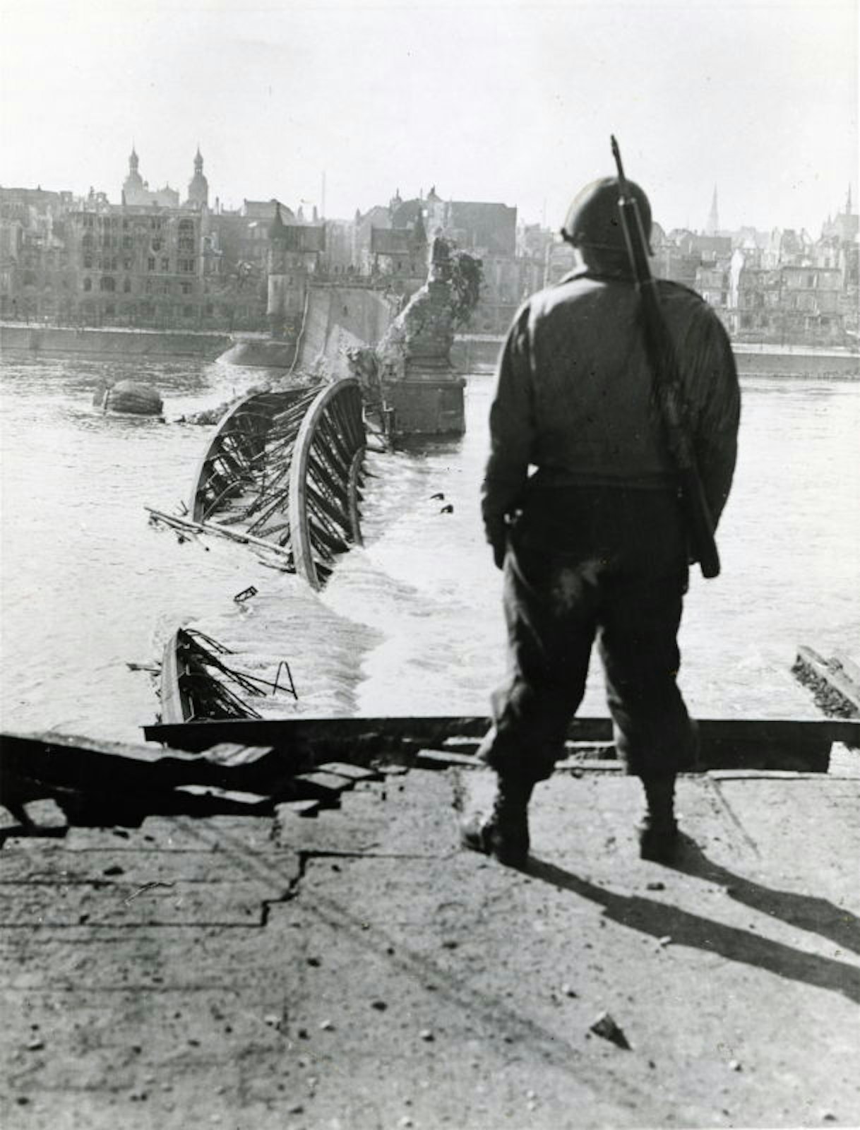 Ein amerikanischer Soldat steht am Brassertufer an der zerstörten alten Rheinbrücke.