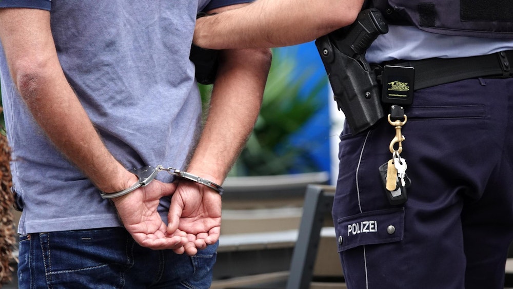 Ein Polizist steht neben einem Mann in Handschellen.