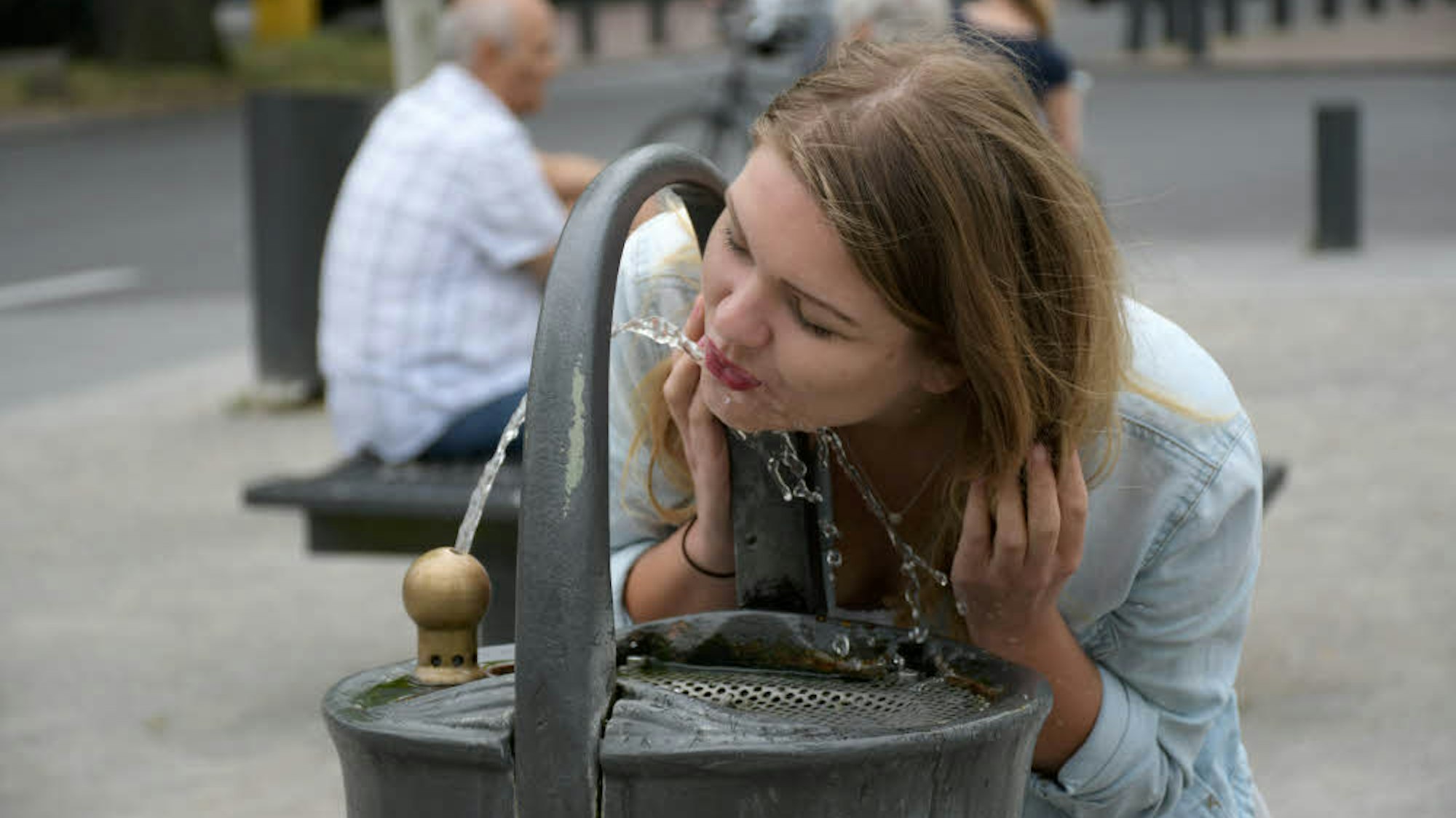Das Foto zeigt eine Frau, die aus einem Trinkwasserbrunnen trinkt.