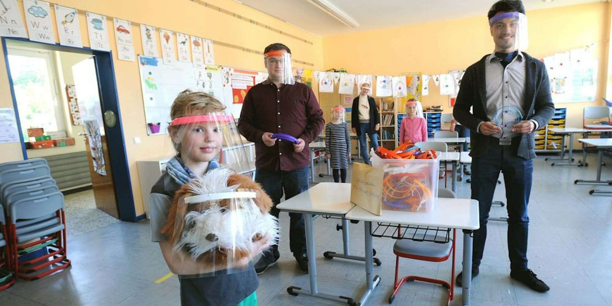 Schülerin Stina Osenberg und Klassenmaskottchen Lino probierten die Gesichts-Visiere aus, die Tobias Siefen (l.) und Mario Mosler (r.) der Grundschule Witzhelden geschenkt haben.