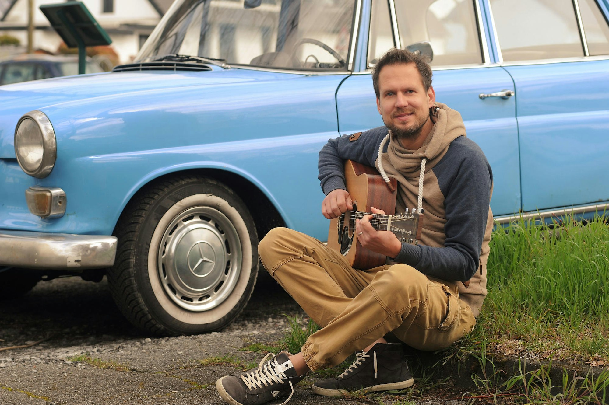 Mike Kremer von Miljö spielt sitzend Gitarre vor einem Auto