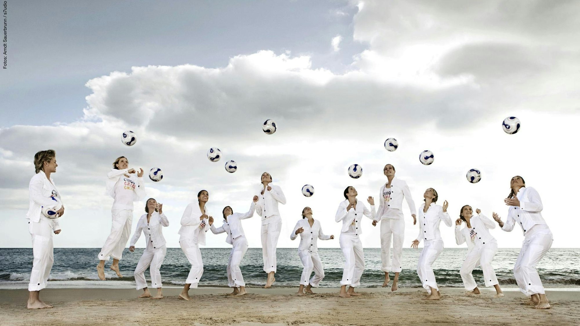 Frauen in weißen Anzügen werfen am Strand Fußbälle in die Luft