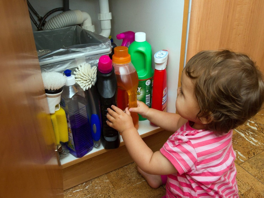 Ein Kind sitzt vor einem Schrank voller Reinigungsmittel.