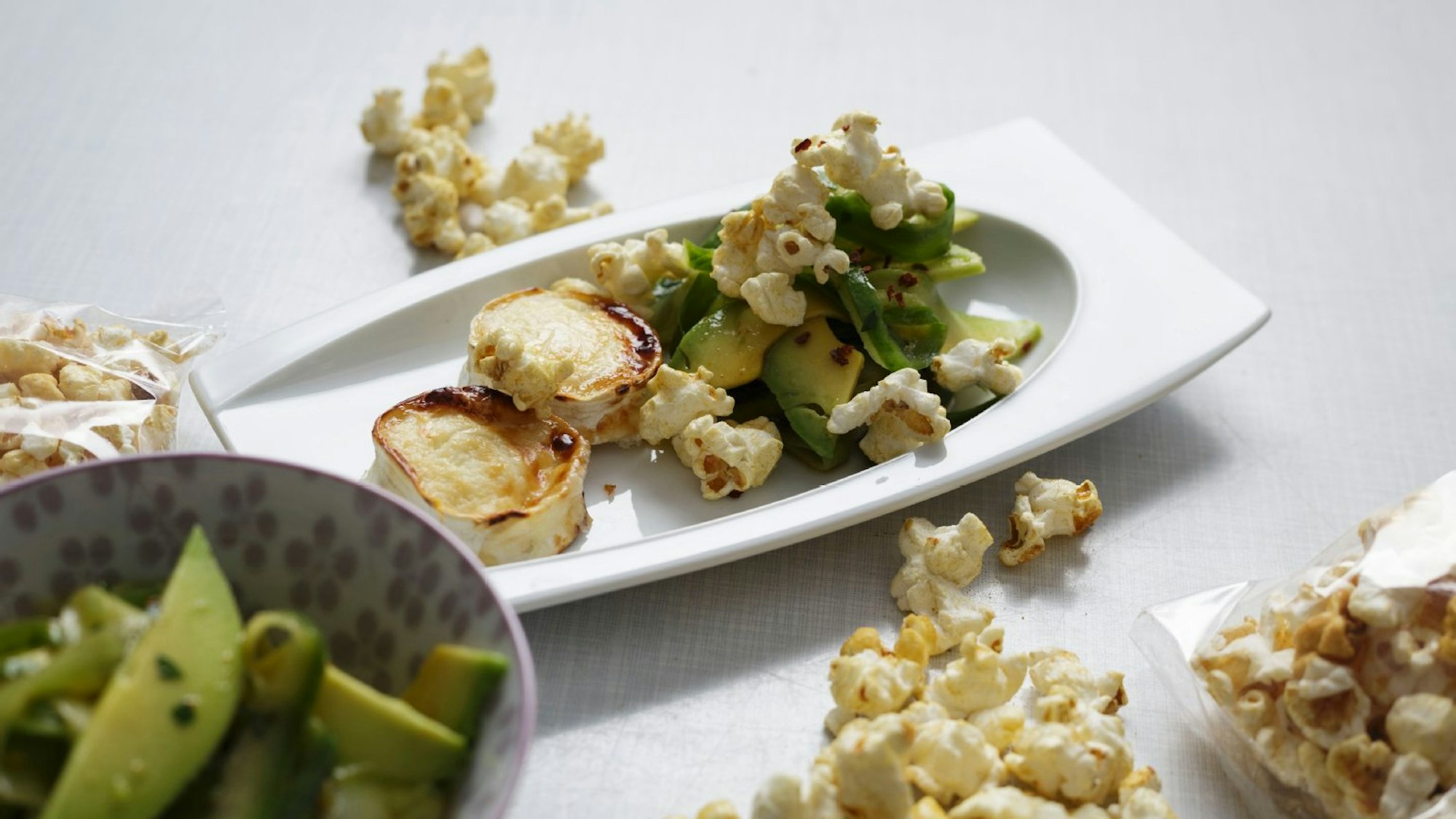Ziegenkäse und Avocado mit Popcorn-Topping auf einem Teller angerichtet
